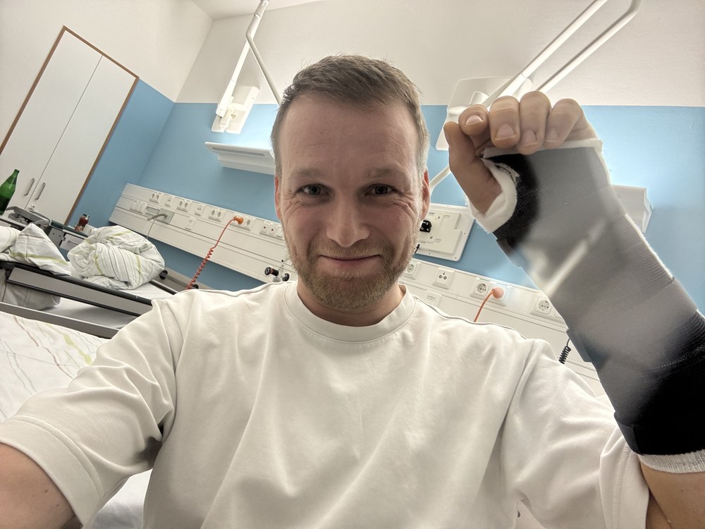Sven in a hospital bed with a cast on his wrist, smiling wryly