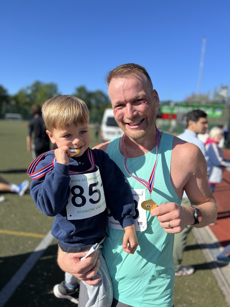 Sven holding his young son, both wearing finisher medals after a race