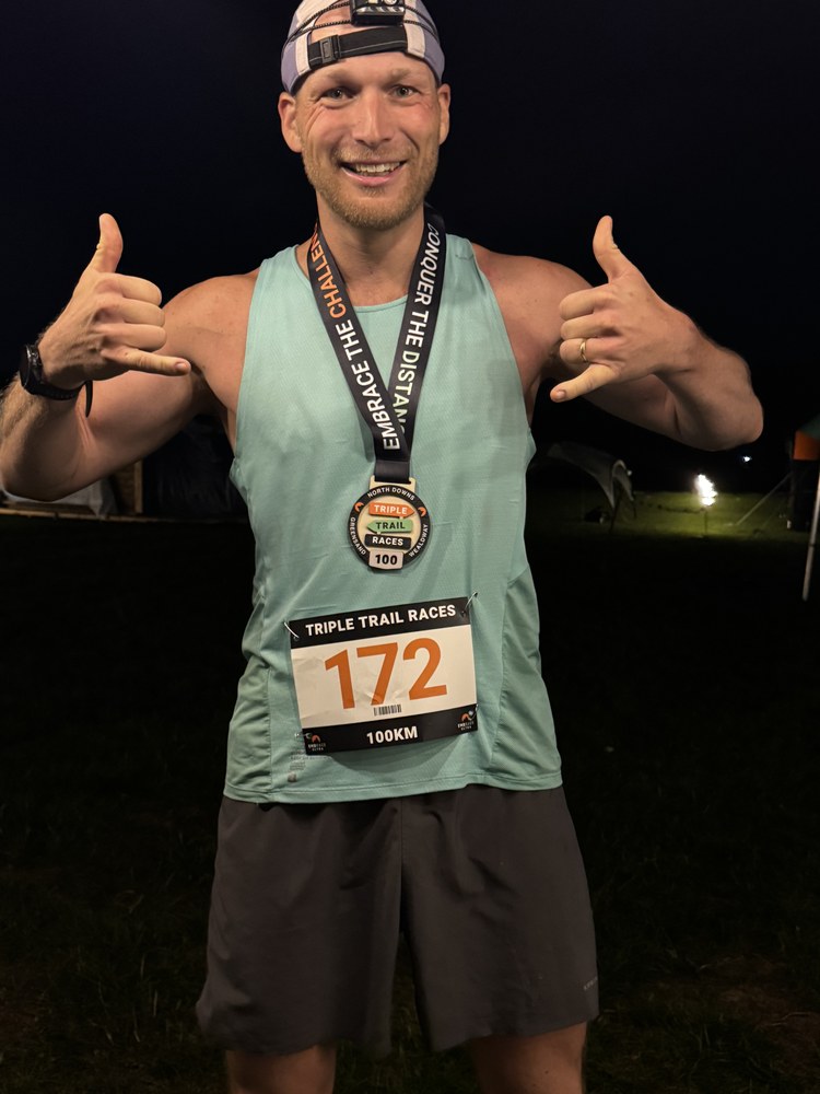 Sven at the finish line at night with a 100 km finisher medal and race bib 172