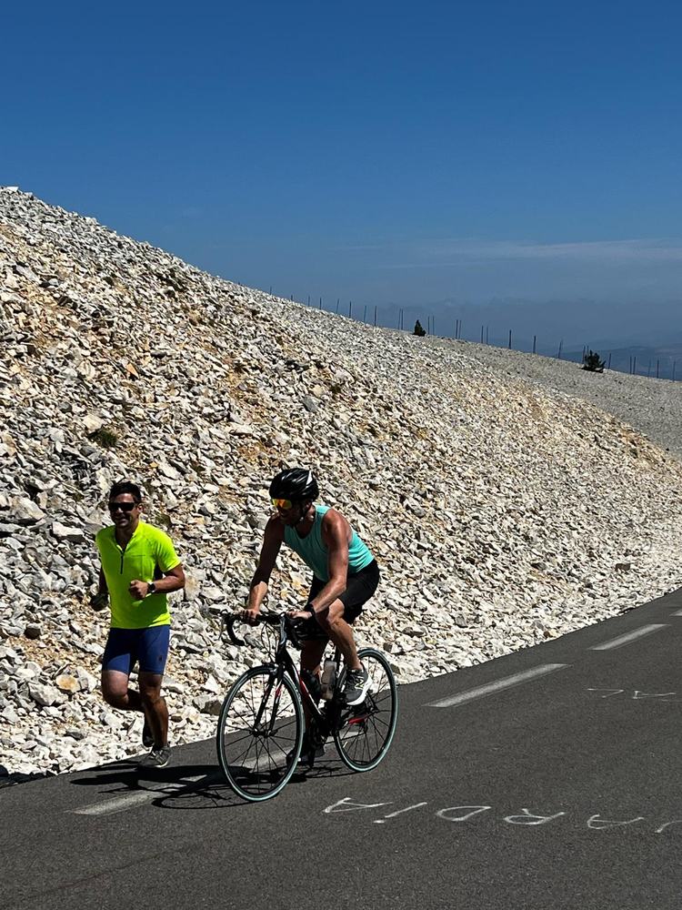 A cyclist and a runner climbing the bare white-rock upper slopes of Mont Ventoux